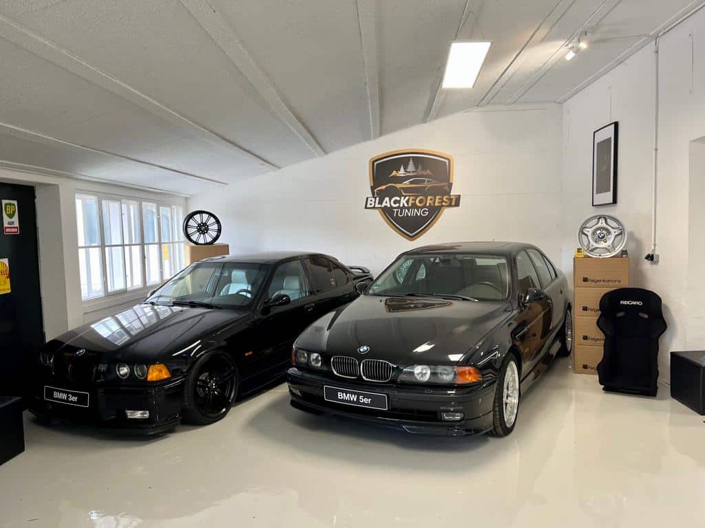 Ein 3er BMW und ein 5er BMW mit dem Blackforest Tuning Logo an der Wand